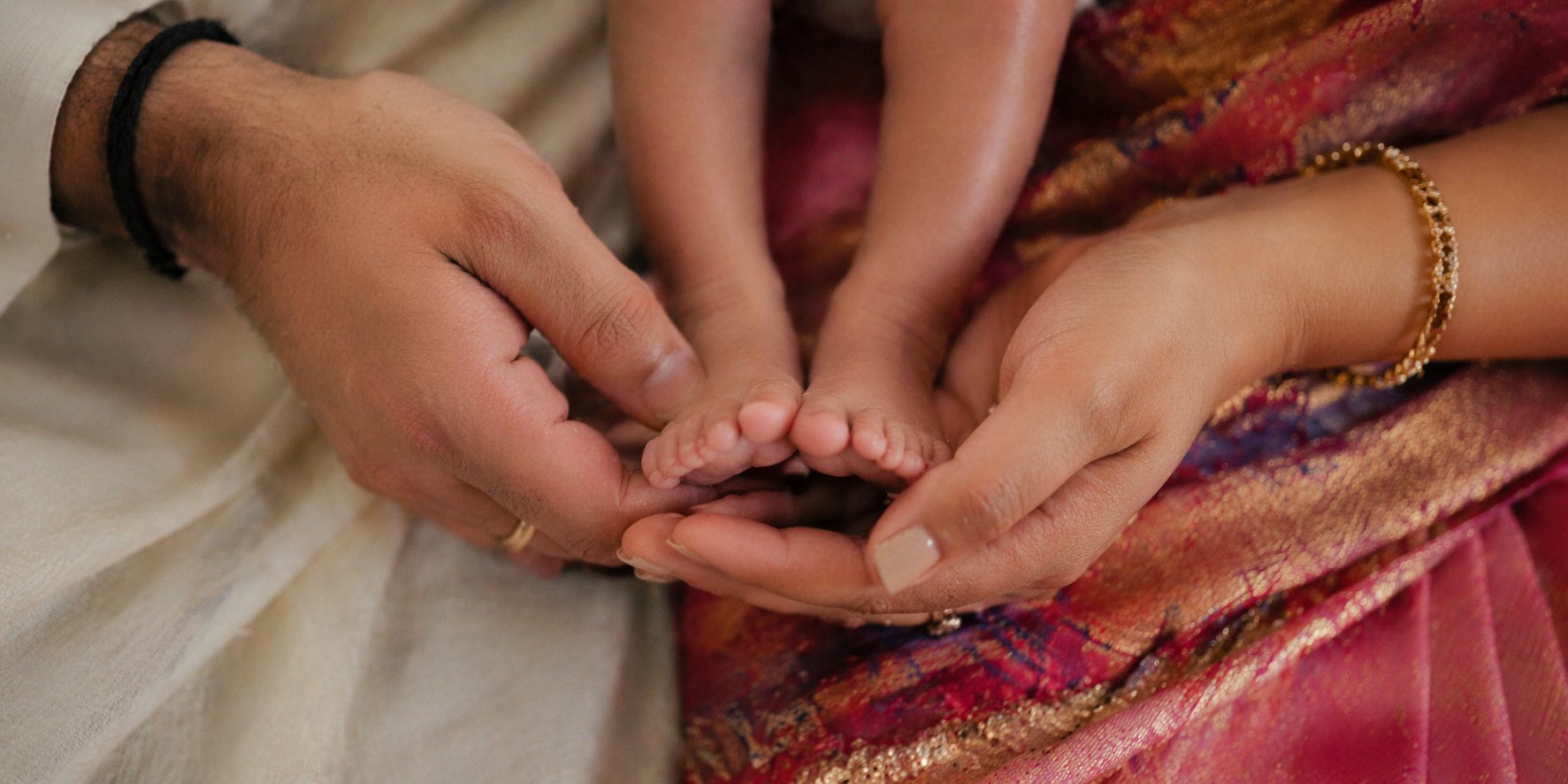 Indian couple's hands cradling newborn baby feet